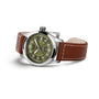 The Hamilton Khaki Field Auto 38mm is a silver wristwatch with a military-inspired design, featuring an olive green face, white numerals, and a brown leather strap—shown angled on a white background.