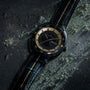 Luxury watch with black leather strap and gold accents on a textured dark surface