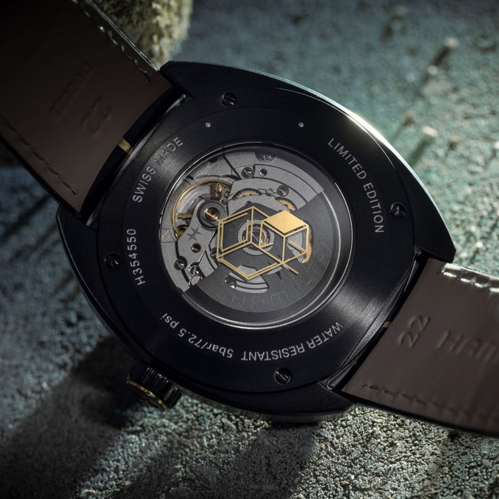 Close-up of a black mechanical watch with a brown leather strap on a textured surface.