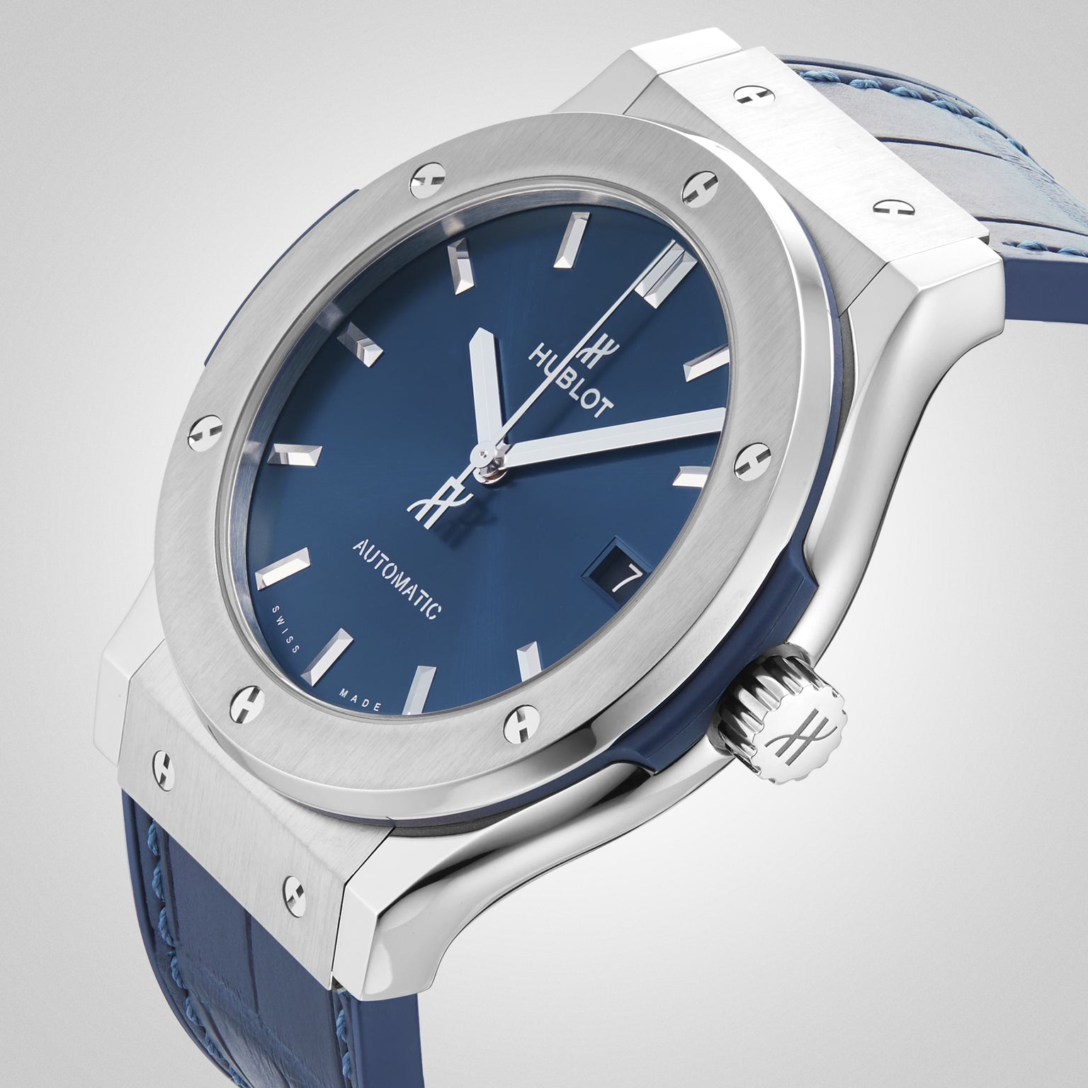 The Hublot Classic Fusion Titanium Blue wristwatch, featuring a blue sunray dial, silver markers, and a blue leather strap, is displayed at an angle on a light background.