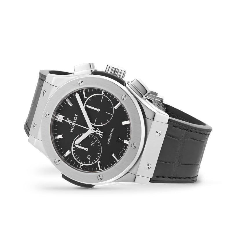 A Hublot Classic Fusion Chronograph Titanium watch with a black dial, three subdials, and a black leather strap is displayed at an angle, highlighting its sleek stainless steel and titanium case.