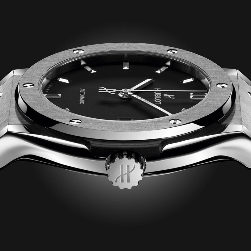 Close-up side view of the Hublot Classic Fusion Titanium wristwatch, showcasing its brushed titanium case, black dial, and metallic crown engraved with the Hublot logo.