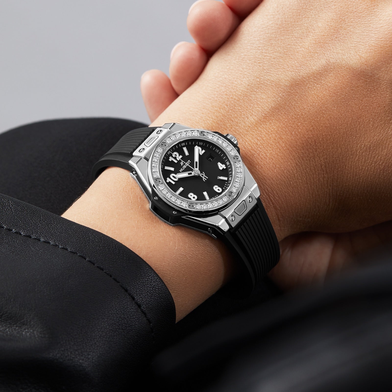 A hand wears a Hublot Big Bang One Click Steel Diamonds watch, featuring a black rubber strap, stainless steel accents, and a black dial displaying the time.