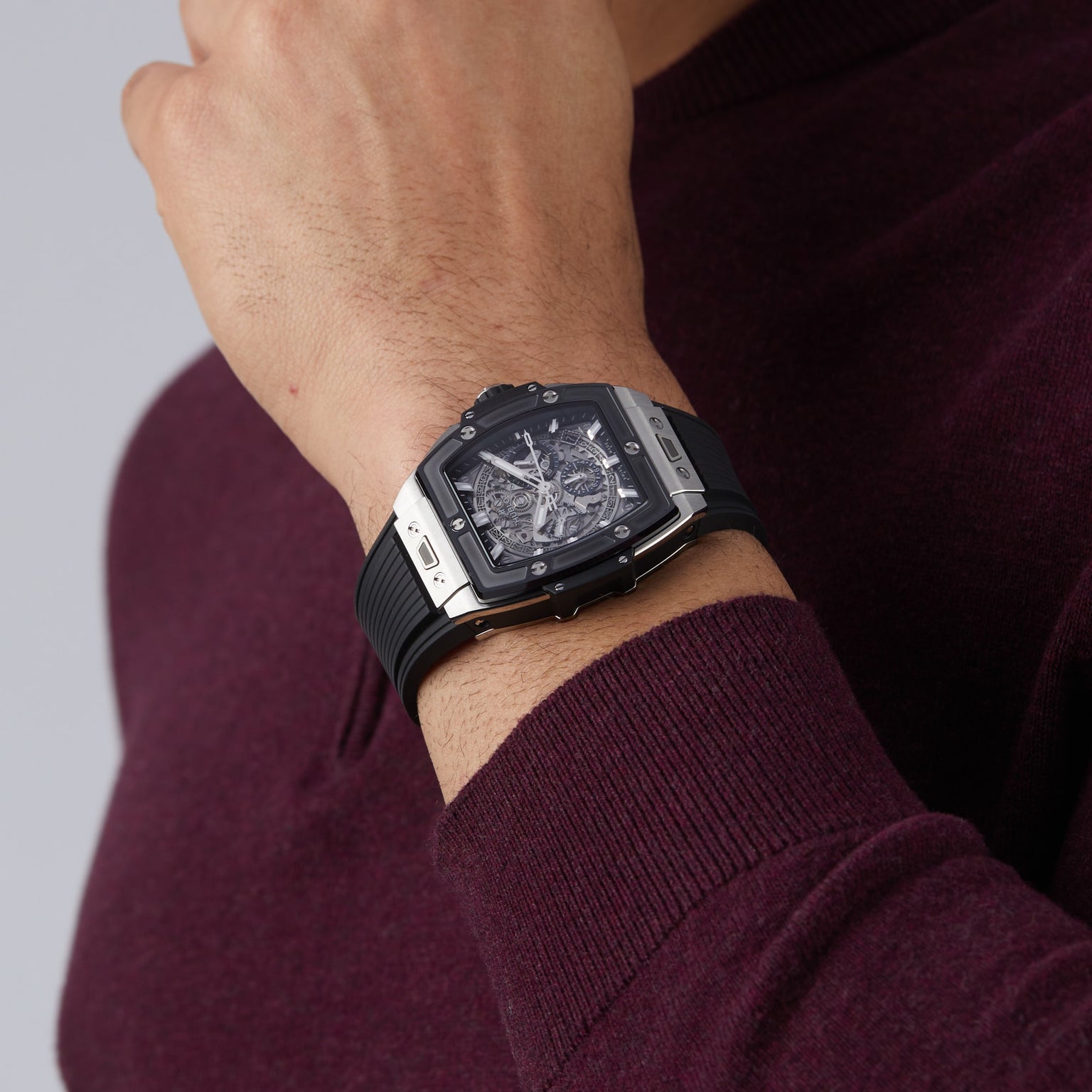 A person wearing a maroon sweater showcases the Hublot Spirit Of Big Bang Titanium Ceramic watch featuring a sapphire crystal dial with a visible mechanical movement on their left wrist.