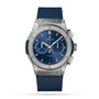 The Hublot Classic Fusion Chronograph Titanium Blue features a titanium case, blue sunray dial with silver markers, chronograph subdials, and a blue rubber strap, shown against a white background.