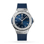 The Hublot Classic Fusion Titanium Blue features a blue dial, titanium case, silver hour markers, date at 3 o’clock, and a blue rubber strap, shown on a white background.