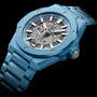 The Hublot Big Bang Integrated Time Only Sky Blue Ceramic features a blue ceramic case, visible automatic movement, silver hour markers, and a metal bracelet, photographed against a black background.
