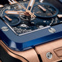 Close-up of the Hublot Square Bang Unico King Gold Blue Ceramic watch with a blue bezel, King Gold case, exposed gears, and visible screws on the bezel.