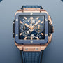The Hublot Square Bang Unico King Gold Blue Ceramic watch features a skeleton dial, King Gold and blue ceramic case, blue rubber strap, and visible chronograph subdials on a light blue background.