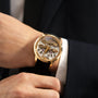 A person in a dark suit wears the Girard-Perregaux Classic Bridges 45, a gold skeleton mechanical wristwatch with a black leather strap, highlighting the precision engineering of this luxury timepiece.