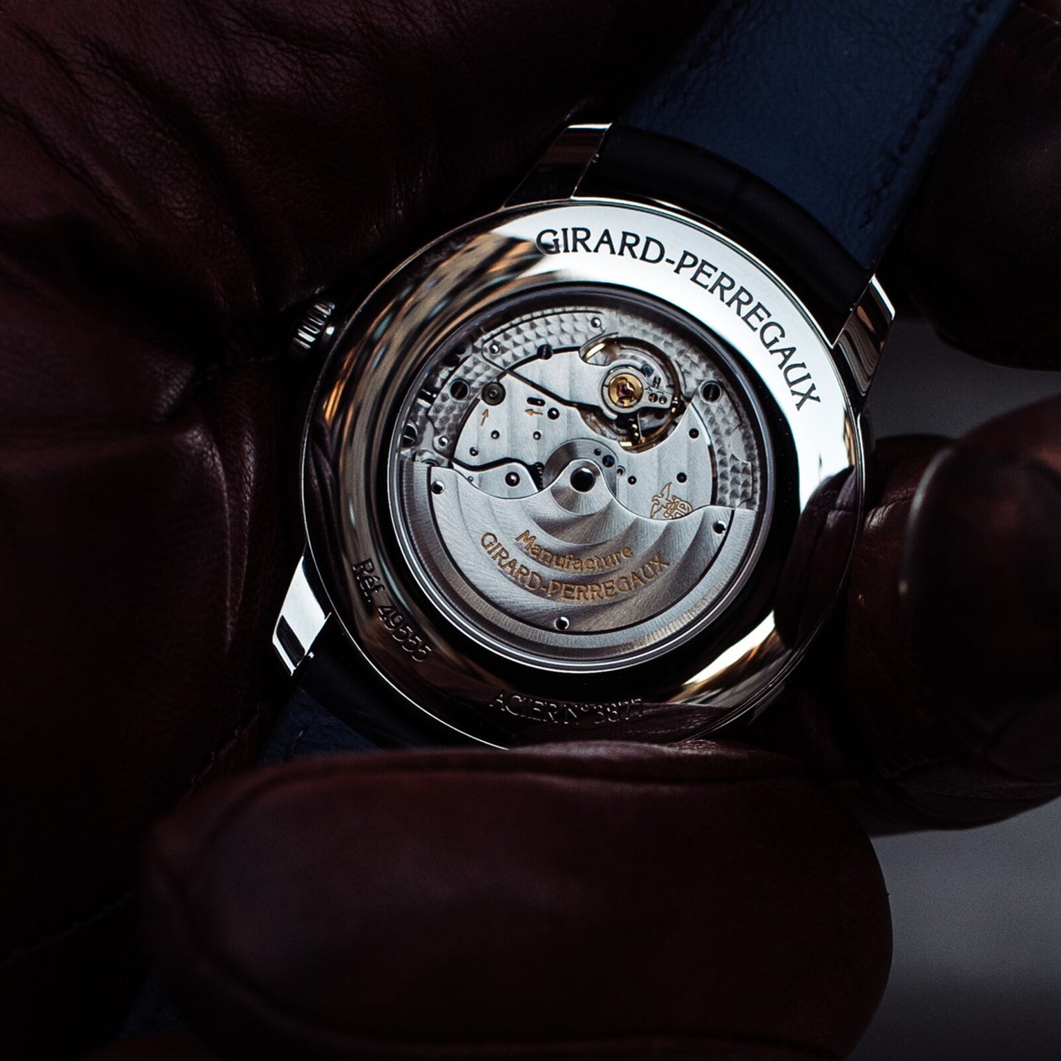A gloved hand holds the Girard-Perregaux 1966 40 wristwatch, displaying the calibre GP0330 movement and engraved brand name through its stainless steel case back.