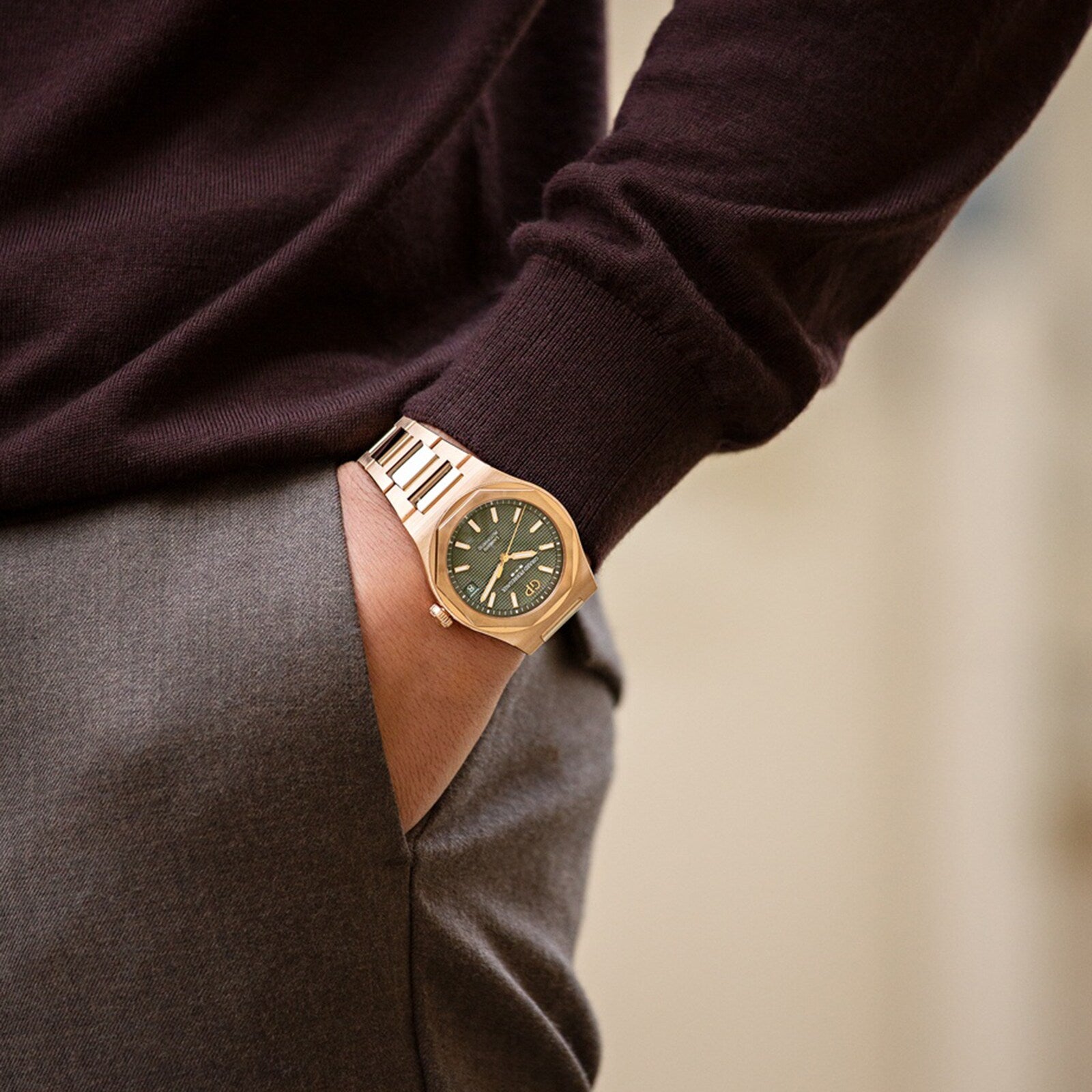 A person wearing a Girard-Perregaux Laureato 42 with a Pink Gold case and Sage Green dial, dressed in a dark long-sleeve shirt and gray pants, stands with one hand in their pocket.