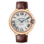 The Ballon Bleu de Cartier by Cartier features a round 18K rose gold case, silver dial with Roman numerals, blue hands, date display, self-winding movement, and brown leather strap.