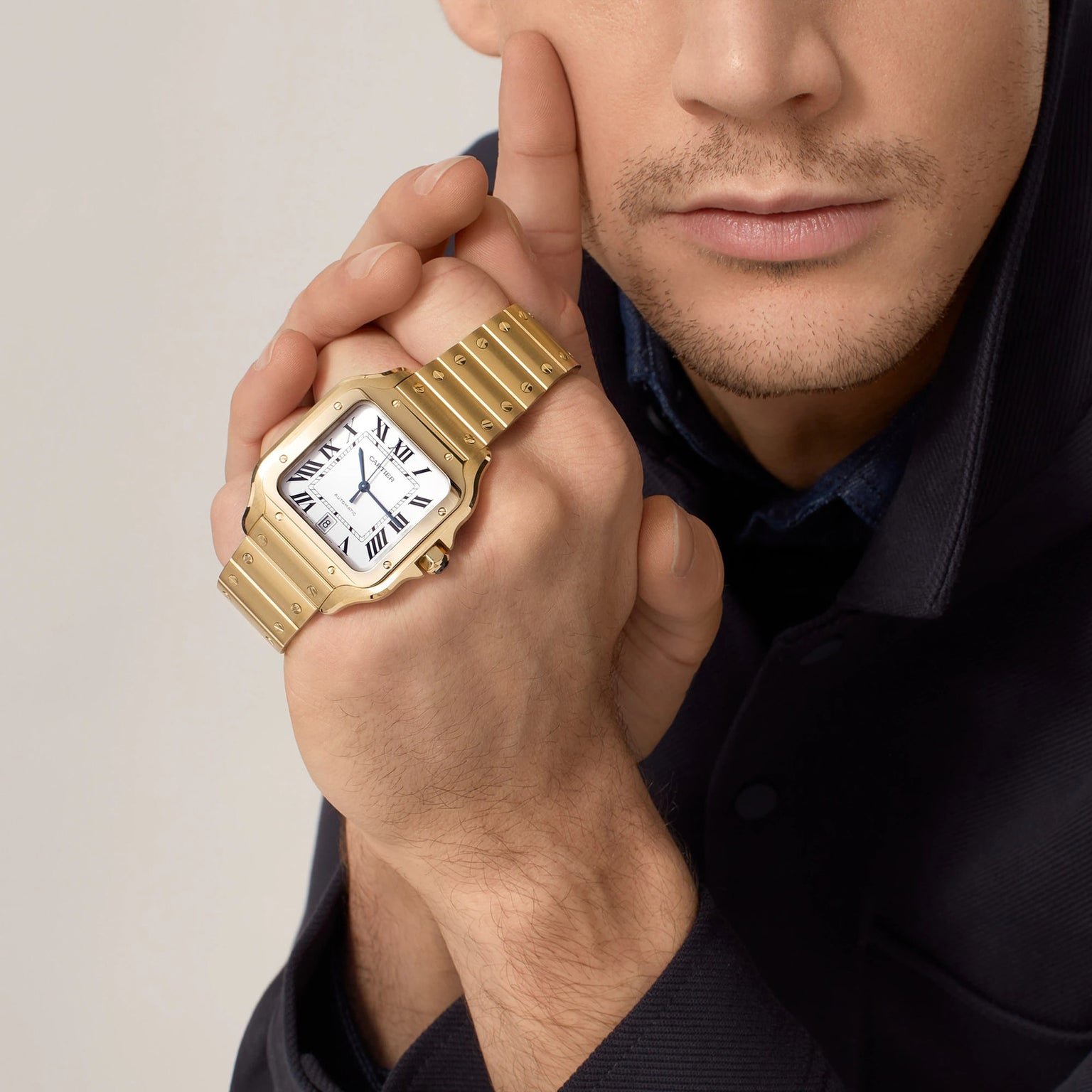 A man in a dark coat holds his wrist near his face, showcasing the Santos de Cartier watch by Cartier with an elegant white dial and classic Roman numerals.