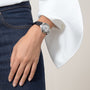 A person wearing blue jeans, a white long-sleeve top, and a Ballon Bleu de Cartier watch with an alligator leather strap by Cartier on their left wrist.
