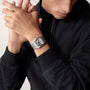 A person wearing a dark zip-up jacket showcases a Cartier Santos de Cartier Skeleton watch with mechanical movement and a square face on their left wrist.