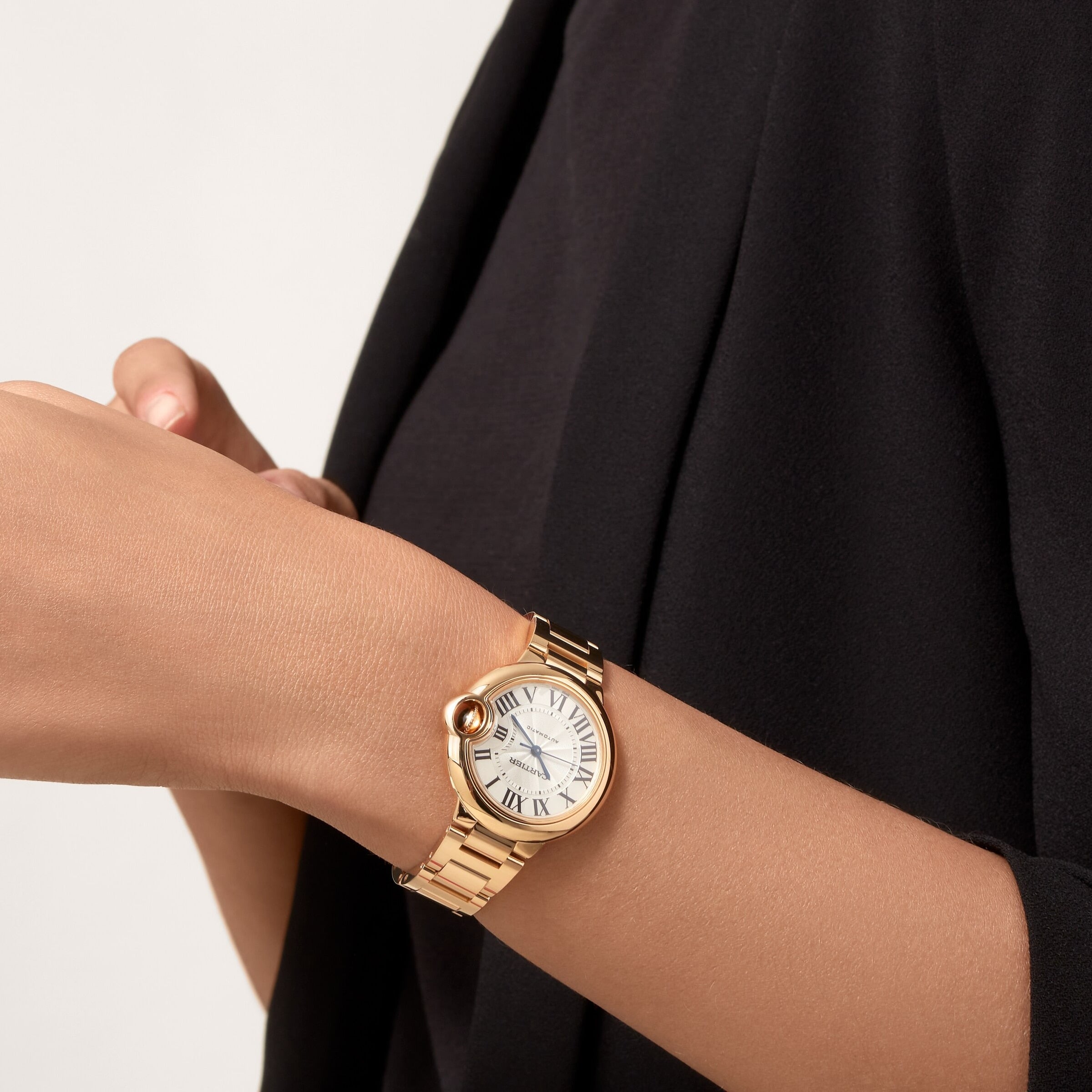 Wearing a Cartier Ballon Bleu de Cartier with yellow gold bracelet and Roman numerals, a person in black adjusts the watch on their left wrist.
