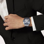 A person in a black suit and white shirt showcases a Cartier Santos de Cartier Skeleton watch with a skeleton design and Manufacture mechanical movement on their left wrist.