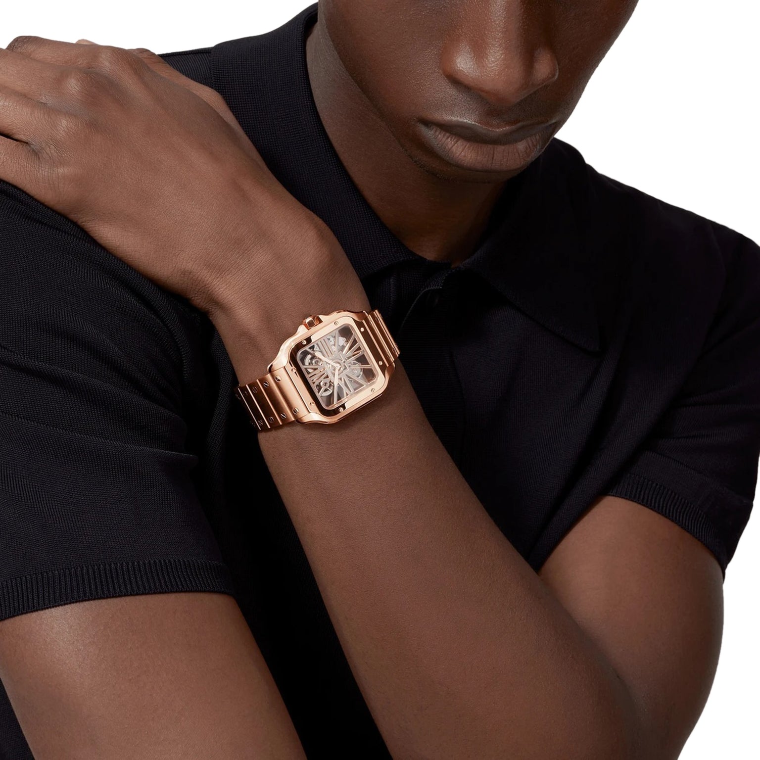 A person in a black short-sleeve shirt wears the Cartier Santos de Cartier Skeleton, featuring a rose gold case, rectangular skeleton dial, and SmartLink adjustment system.