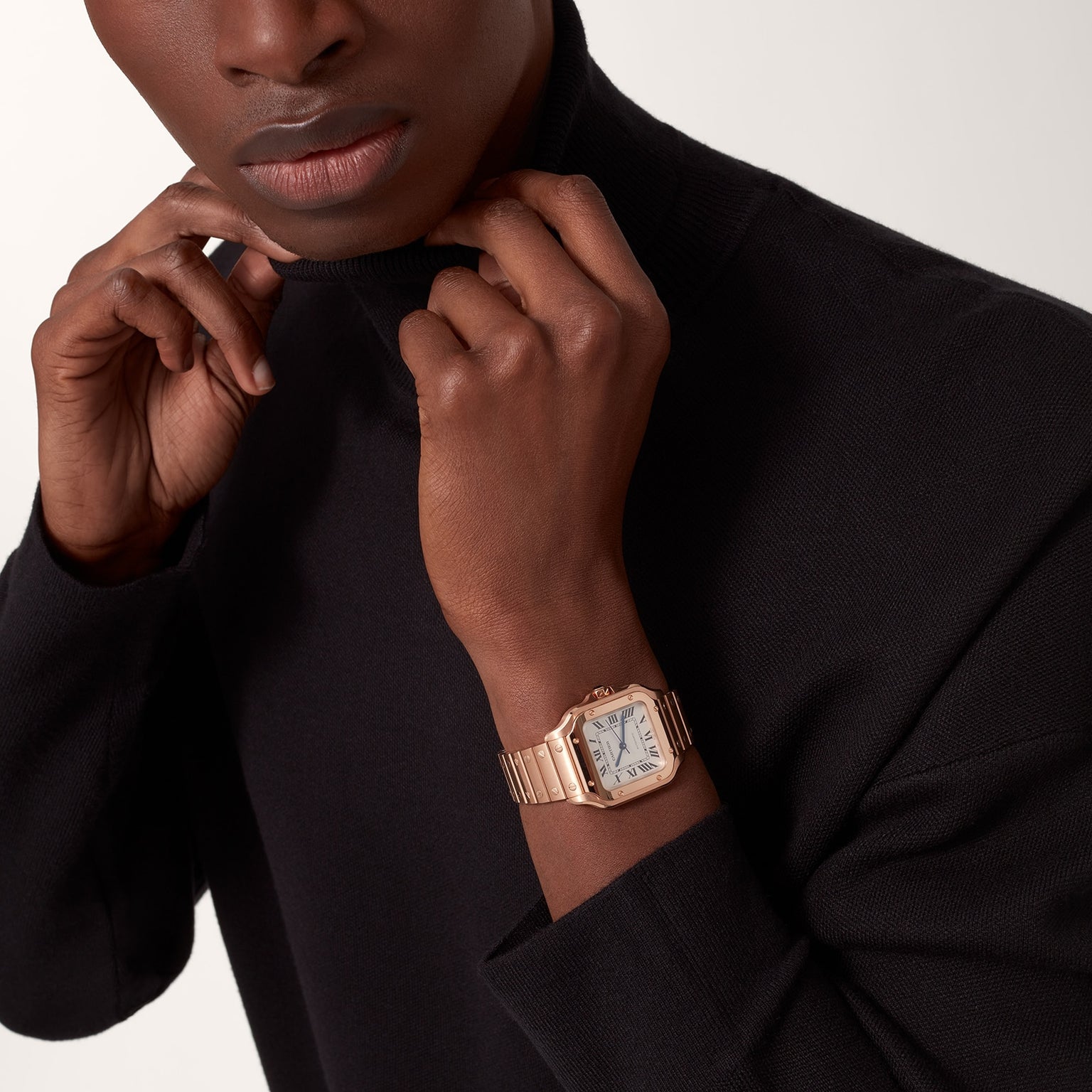 Person wearing a black turtleneck and a rose gold Cartier Baignoire watch, adjusting the sweater collar against a neutral backdrop.