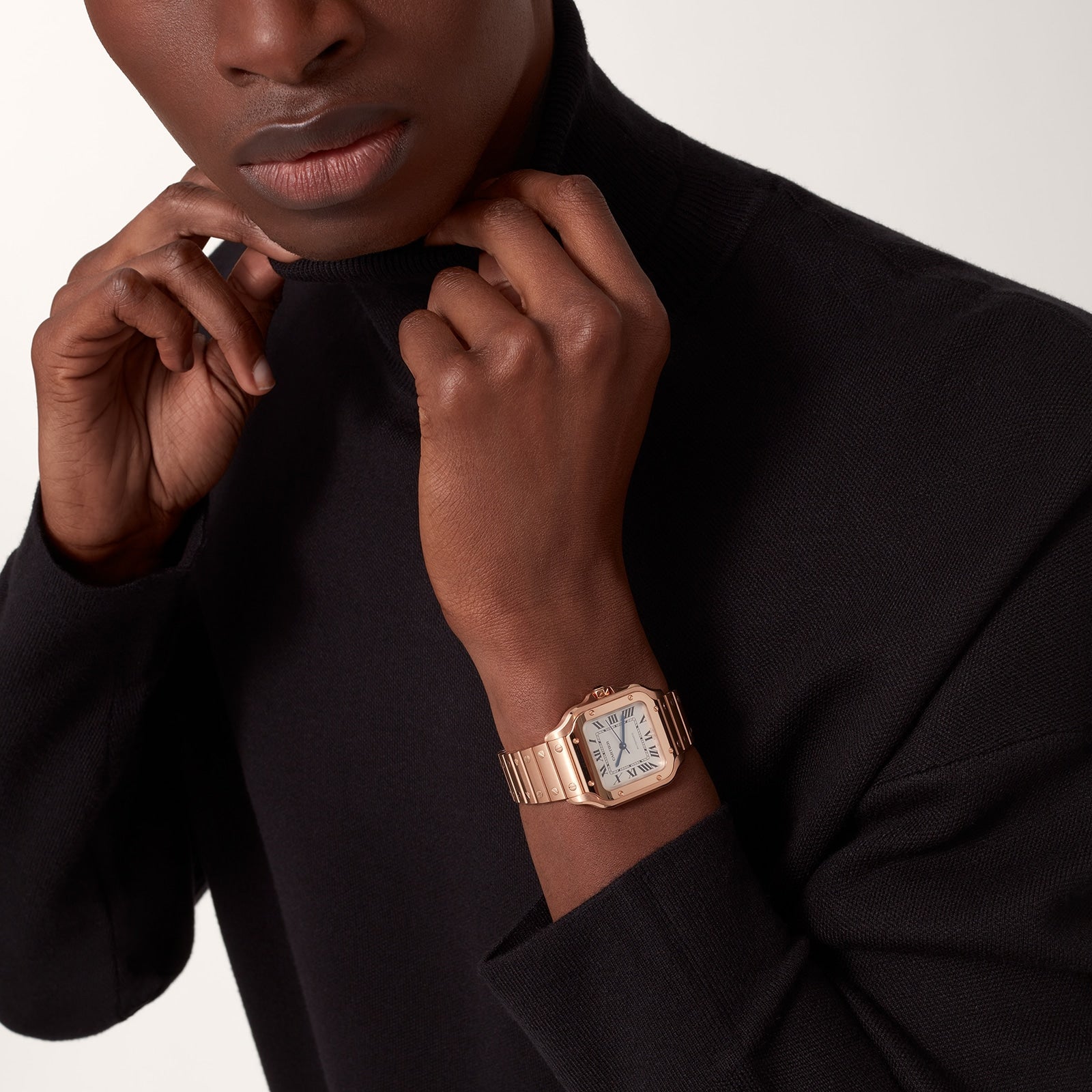 Person wearing a black turtleneck and a rose gold Cartier Baignoire watch, adjusting the sweater collar against a neutral backdrop.