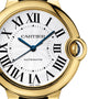 Close-up of the Cartier Ballon Bleu de Cartier watch featuring Roman numerals, blue hands, a detailed silver-white dial, and a partially enclosed crown in a yellow gold case.