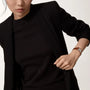 A woman in a black outfit adjusts her blazer, showcasing the Cartier Tank Louis Cartier watch with a rose gold case and alligator strap on her wrist.