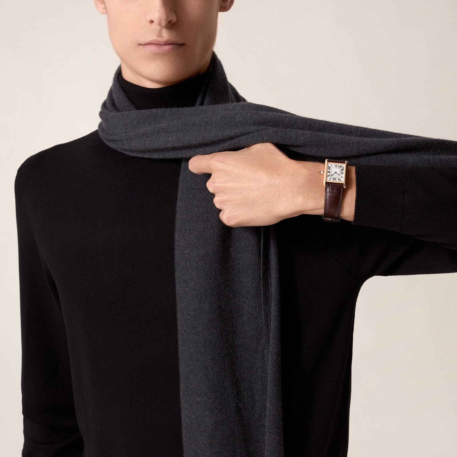 A person in a black turtleneck and dark scarf showcases a Cartier Tank Louis Cartier watch with a brown leather strap and rose gold case on their left wrist.