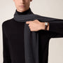 A person in a black turtleneck and dark scarf showcases a Cartier Tank Louis Cartier watch with a brown leather strap and rose gold case on their left wrist.