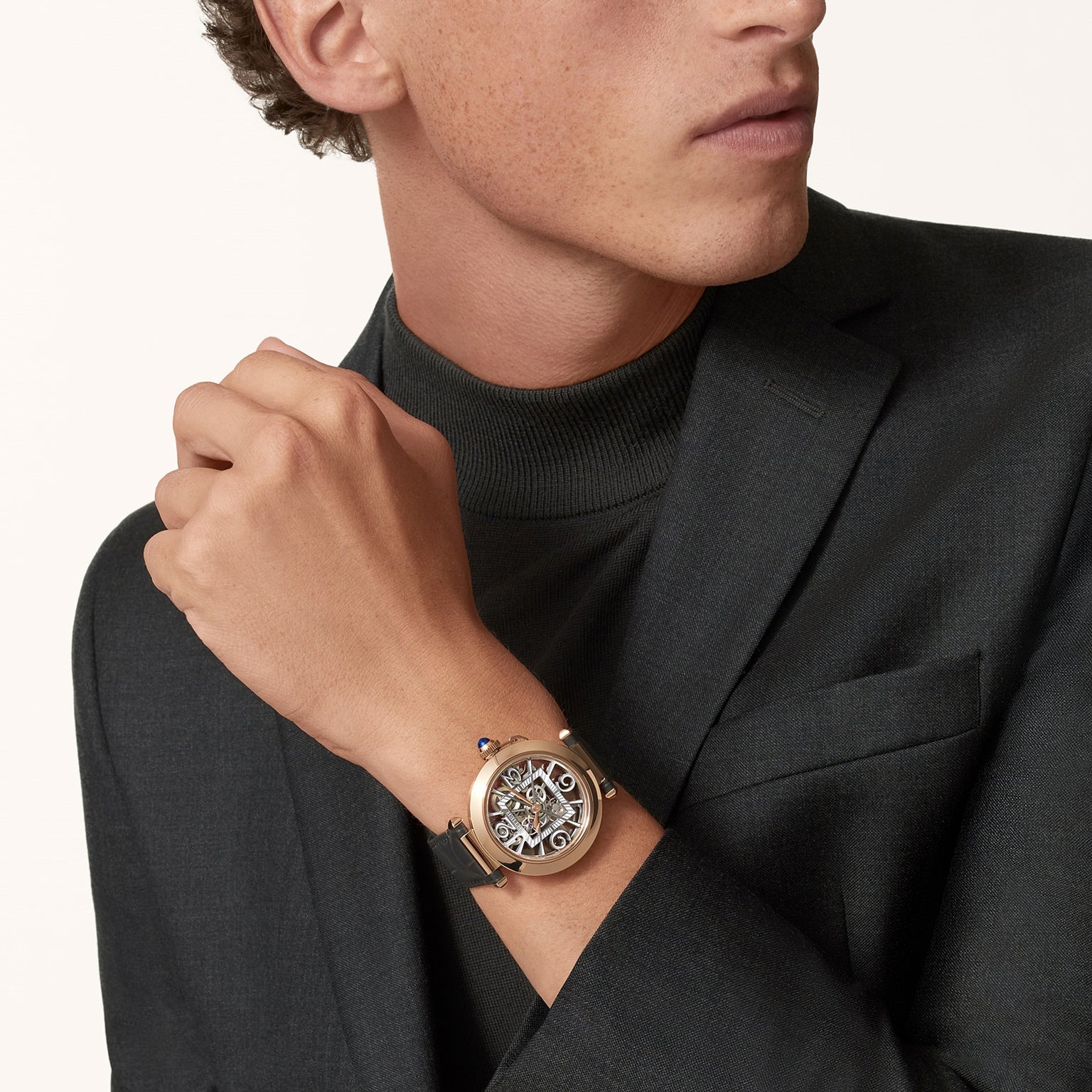 A man in a dark suit displays the Pasha de Cartier luxury skeleton watch by Cartier on his wrist, set against a neutral background.