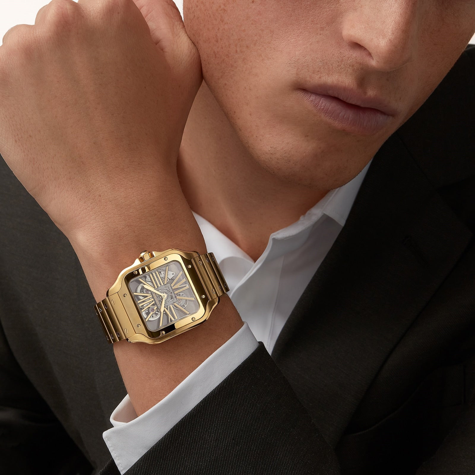 A person in a suit wears a Cartier Santos de Cartier Skeleton wristwatch with a rectangular face and Roman numerals.
