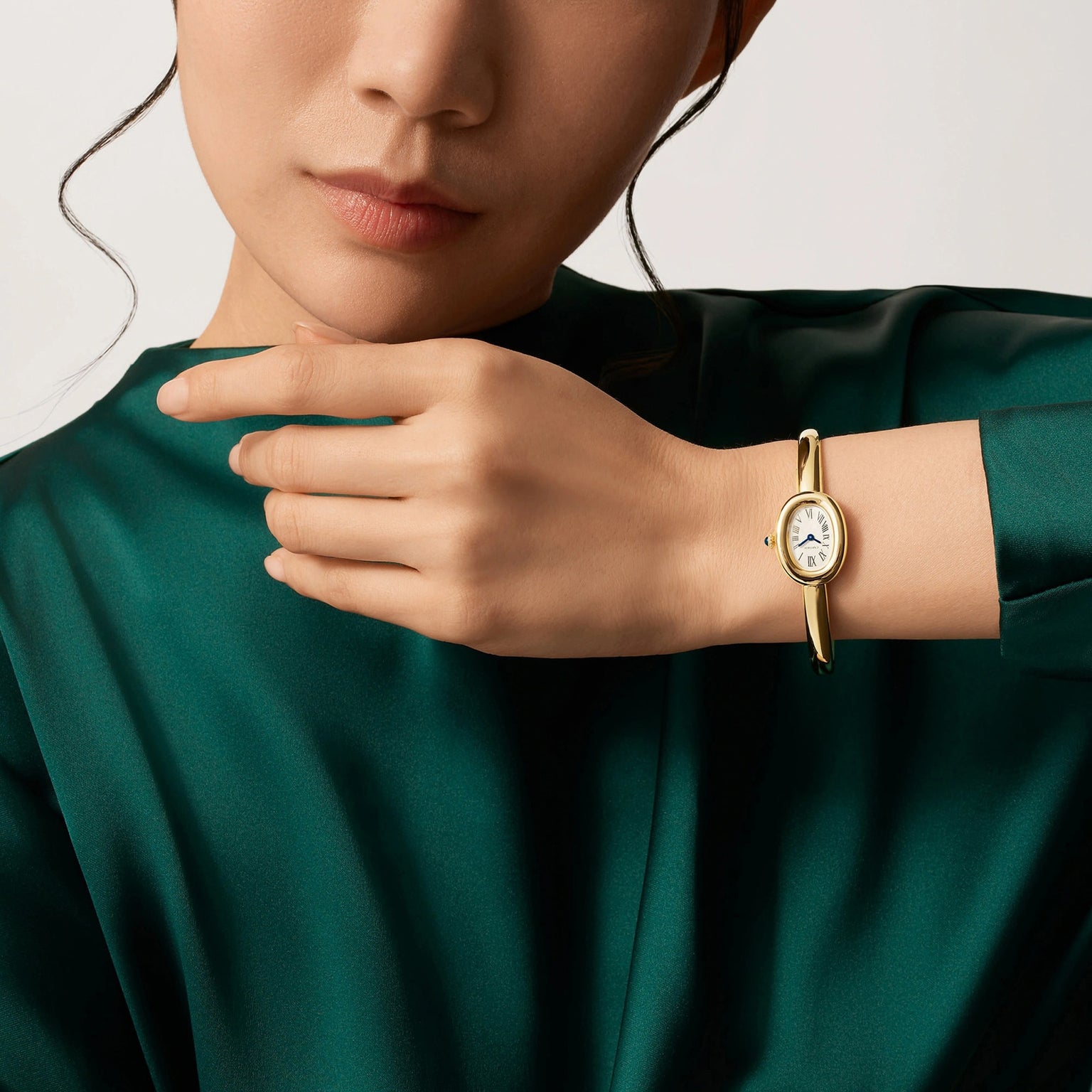 A woman in a green top wears a Cartier Baignoire (Size 17) gold wristwatch, touching her wrist with her other hand.