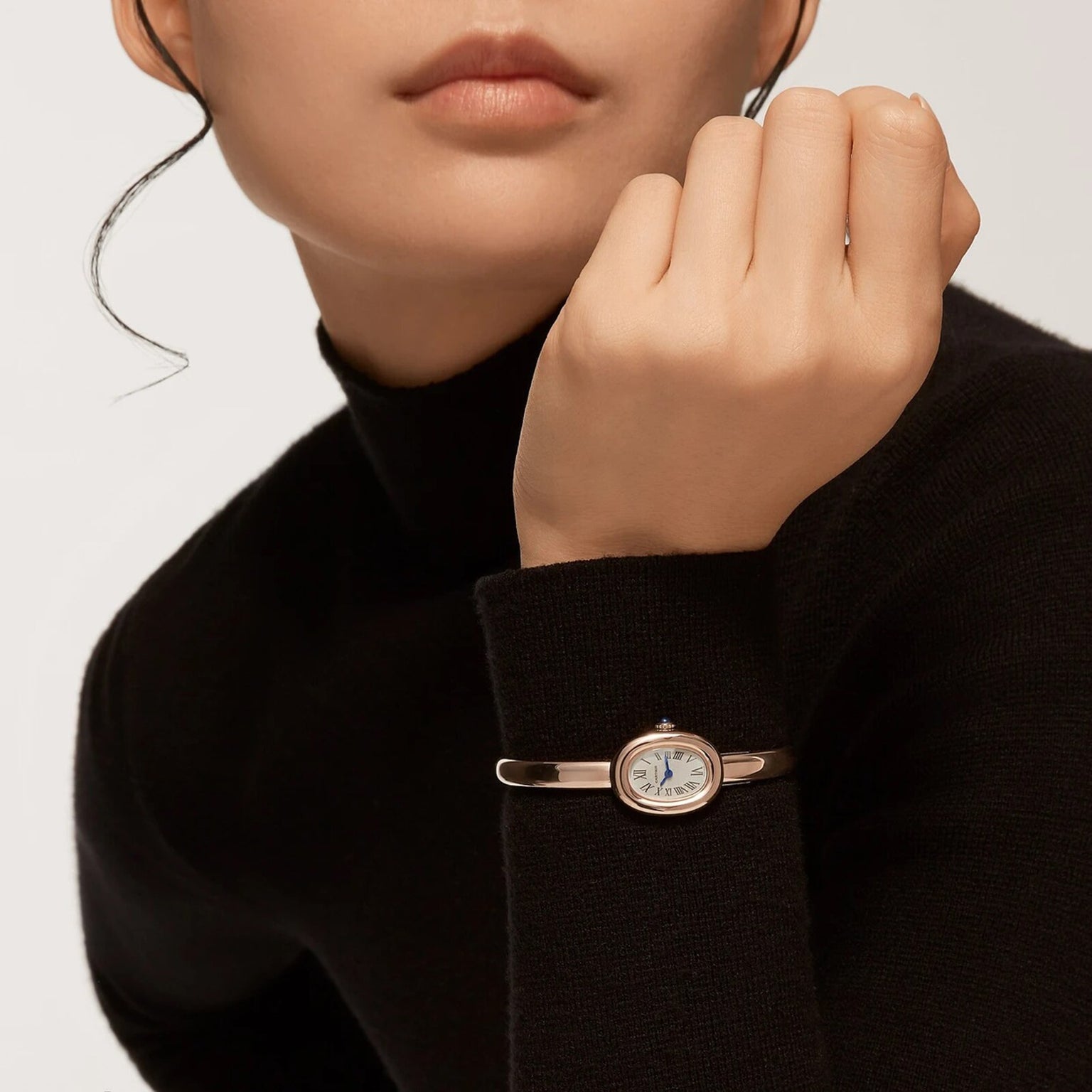 A woman in a black turtleneck wears a Cartier Baignoire (Size 17) gold wristwatch, resting her chin on her hand.