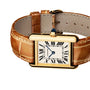 The Cartier Tank Louis Cartier watch features a yellow gold case, tan leather strap, Roman numeral markers, and a blue sapphire cabochon on the crown, shown against a white background.