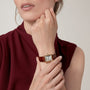 A woman in a sleeveless burgundy top displays her Cartier Tank Louis Cartier watch with a yellow gold case and brown leather strap on her left wrist.