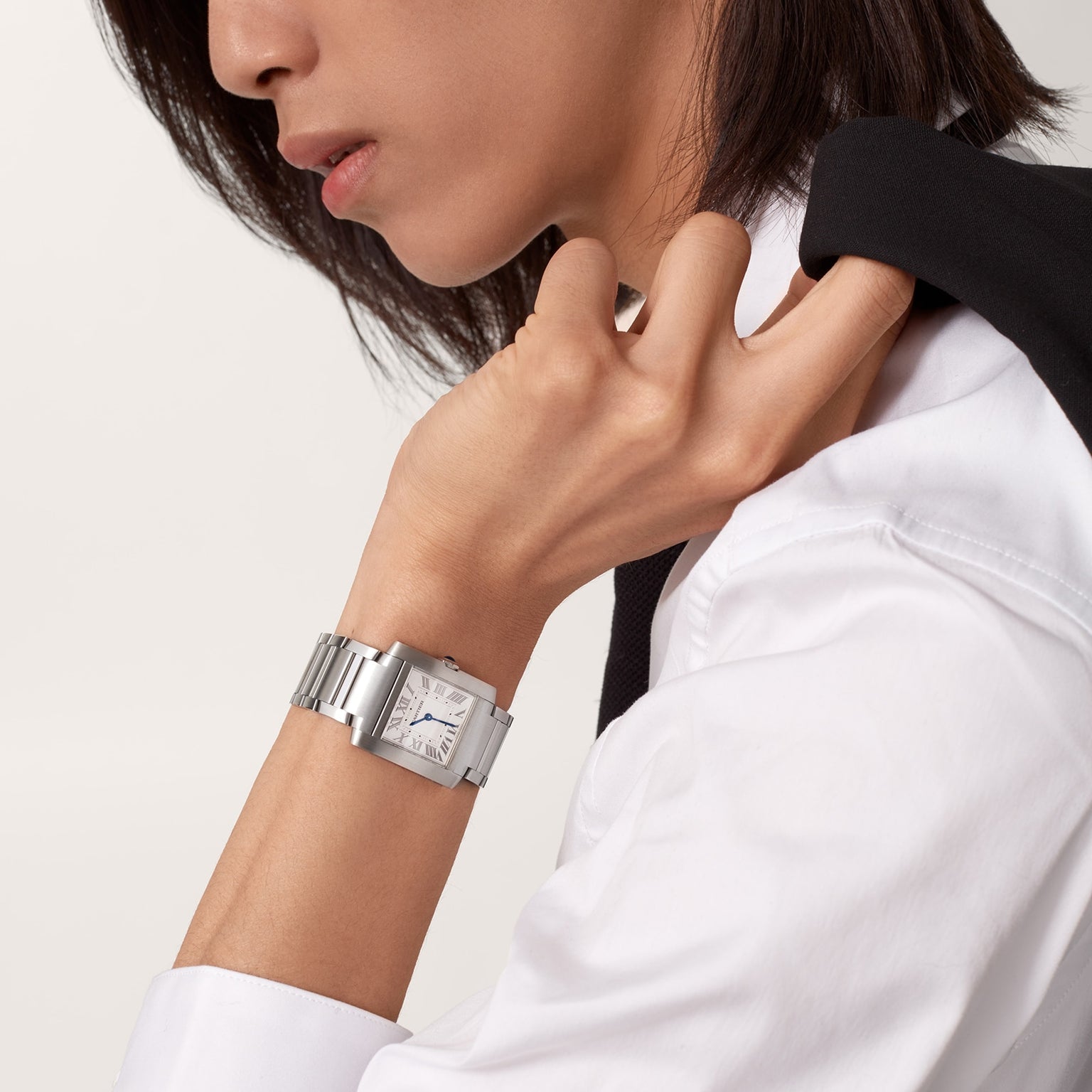 Person in a white shirt with a black jacket over their shoulder, wearing the Cartier Tank Française watch on their left wrist.