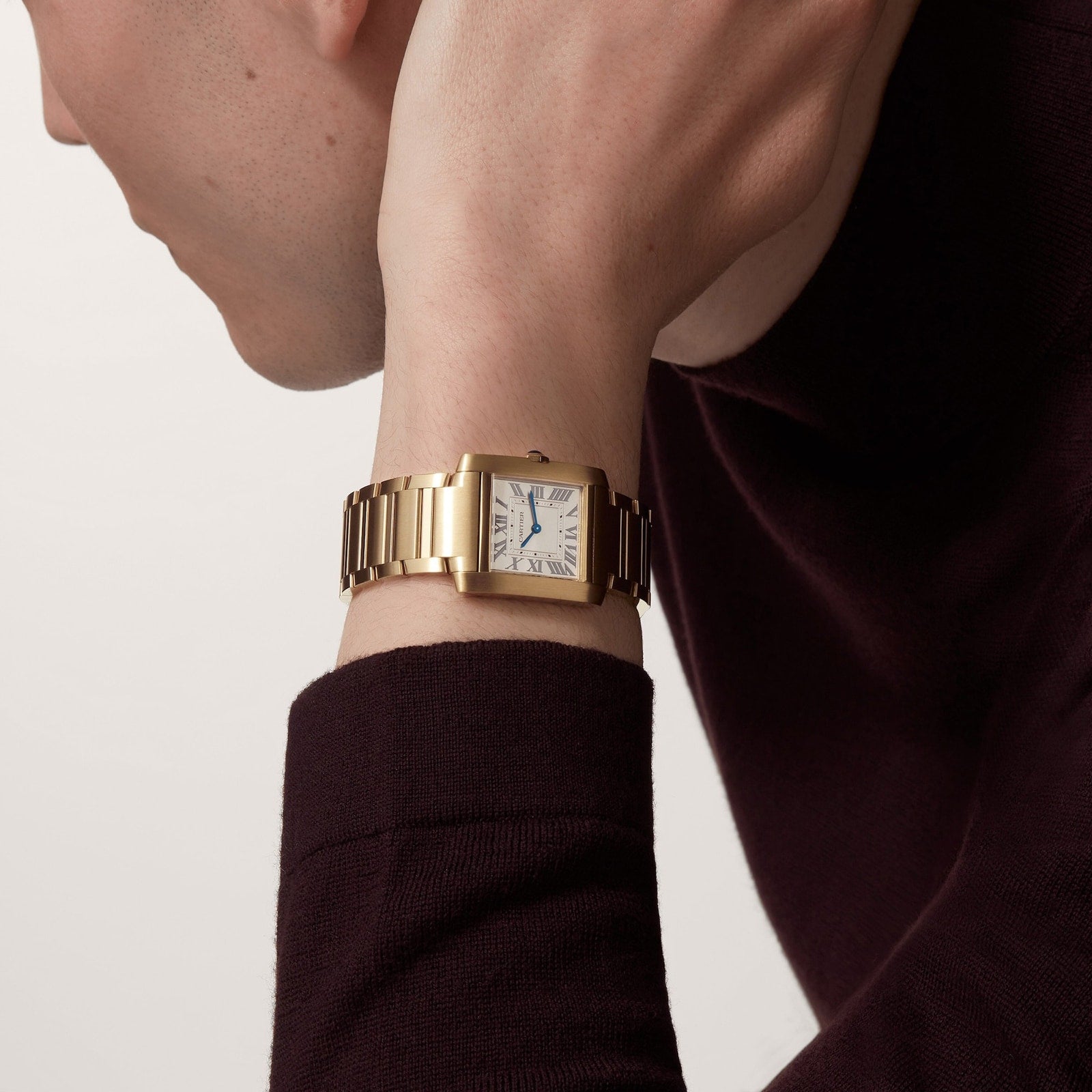 A person wearing a Cartier Tank Française with Roman numerals and a white dial on a yellow gold bracelet, paired with a dark long-sleeve top.