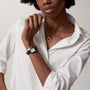 A person wearing a white button-up shirt, gold jewelry, and a square-faced Cartier Tank Must de Cartier watch with quartz movement poses with one hand near their neck.