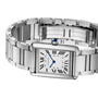 The Cartier Tank Must Solarbeat™ features a stainless steel rectangular case, white dial with black Roman numerals, blue hands, metal bracelet, and a blue gemstone set in the crown.