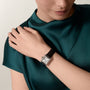 A person in a green satin top wears the Cartier Tank Must de Cartier watch, featuring a rectangular steel case and black leather strap, on their left wrist.