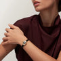 A woman in a burgundy top touches her shoulder while wearing a Cartier Baignoire gold and black wristwatch.