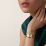 A person wearing a Cartier Tank Française with a yellow gold rectangular case rests their hand near their neck, paired with a dark green sleeveless top.