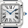 Close-up of a Cartier Santos-Dumont watch face with Roman numerals, blue hands, a silver bezel, and a blue cabochon crown on the right.