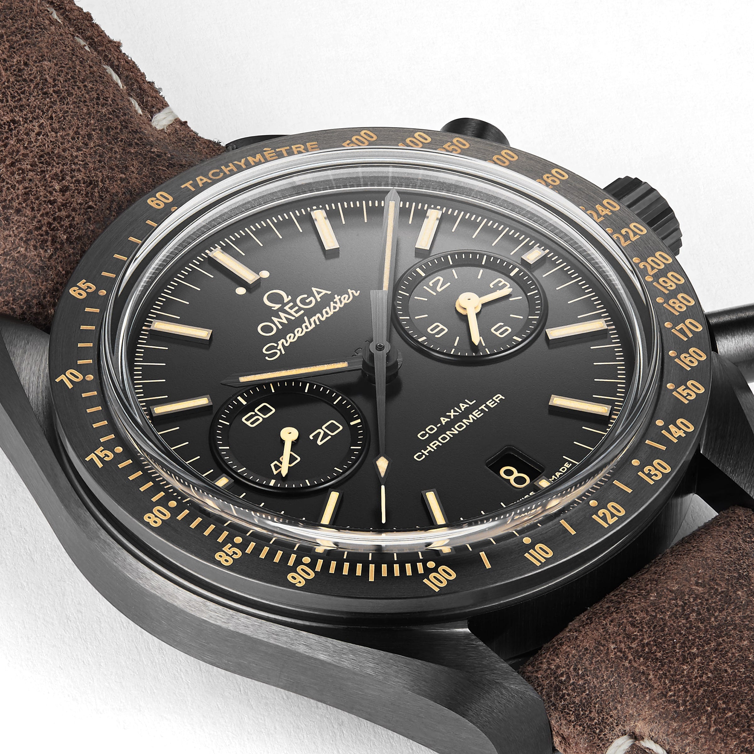Close-up of the OMEGA Speedmaster Dark Side Of The Moon featuring a black dial with gold accents, chronograph subdials, a tachymeter bezel, brown leather strap, and powered by the 9300 calibre movement.