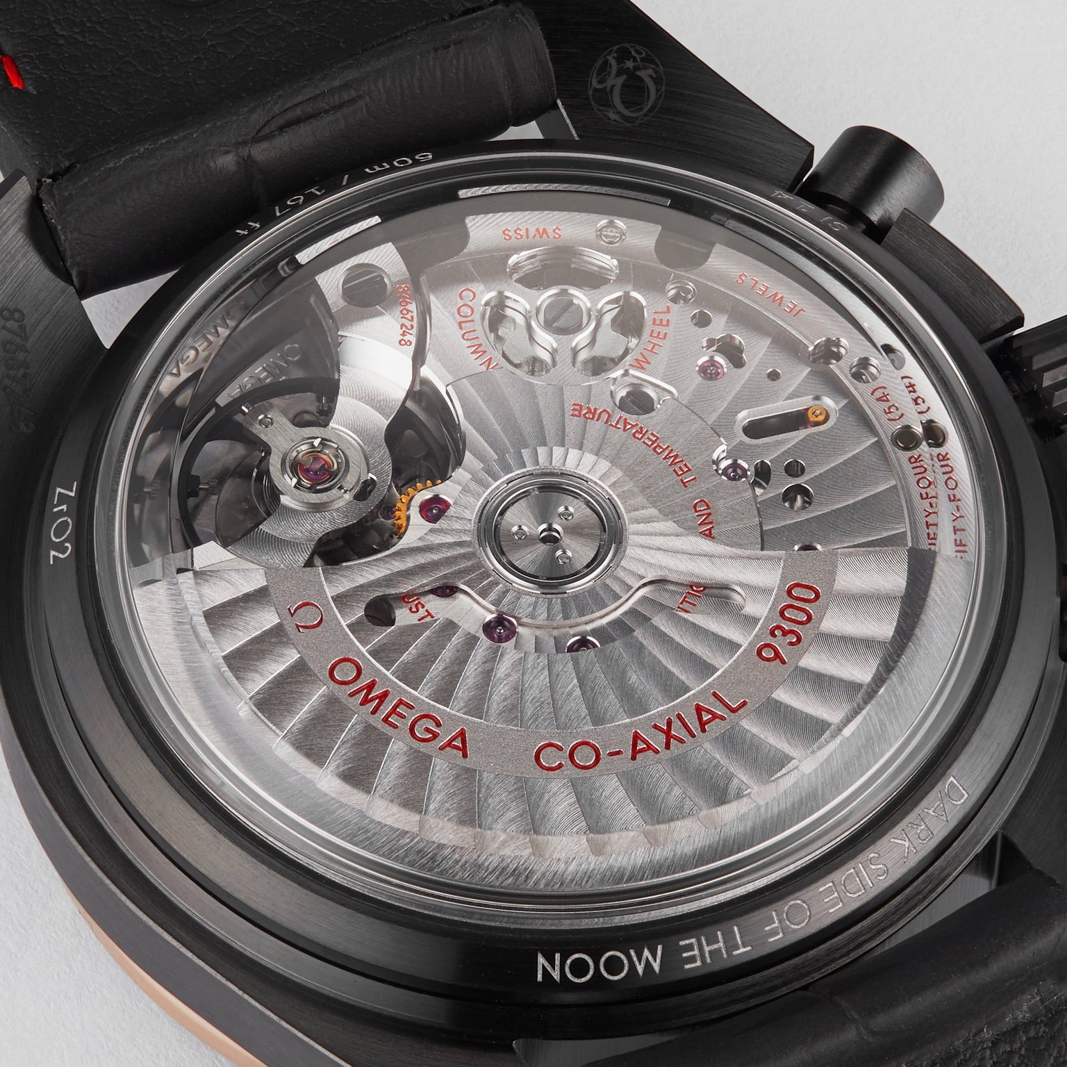 Close-up of the OMEGA Speedmaster Dark Side Of The Moon Sedna Black, showcasing its intricate mechanical movement and engraved details through a transparent case back set within a sleek black ceramic casing.