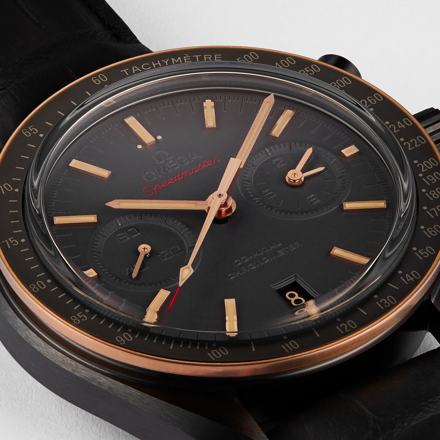 Close-up of the OMEGA Speedmaster Dark Side Of The Moon Sedna Black, featuring a black ceramic dial, gold accents, two subdials, tachymeter scale, and a date window at 6 o’clock.
