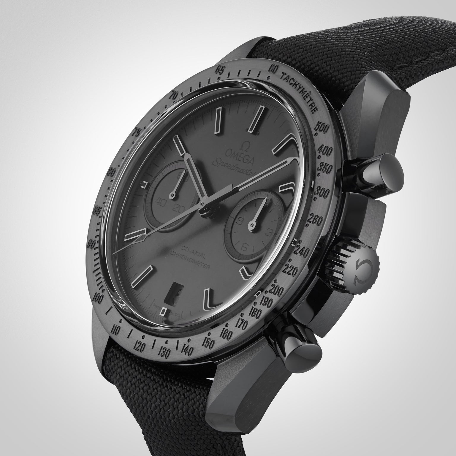 The OMEGA Speedmaster Dark Side of the Moon Black Black chronograph, featuring a black fabric strap, is displayed at an angle against a neutral background.