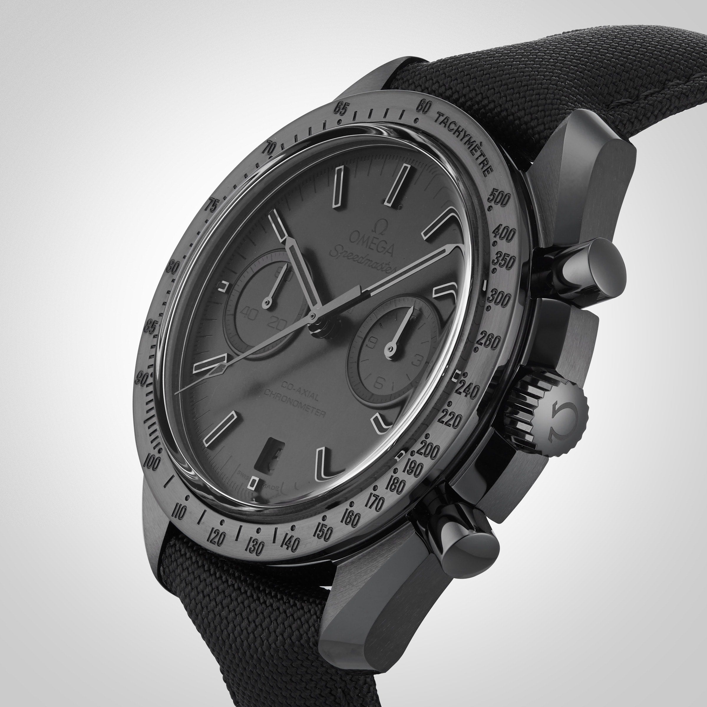 The OMEGA Speedmaster Dark Side of the Moon Black Black chronograph, featuring a black fabric strap, is displayed at an angle against a neutral background.