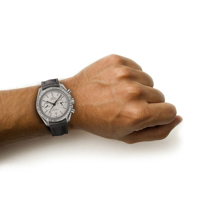 A person wearing an OMEGA Speedmaster Dark Side of the Moon wristwatch with a black leather strap on their left wrist against a white background.