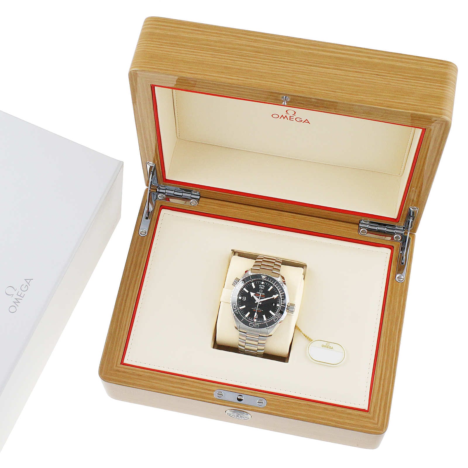An OMEGA Seamaster Planet Ocean 600M stainless steel dive watch is shown in an open wooden presentation box with a cream interior, next to a white branded box.